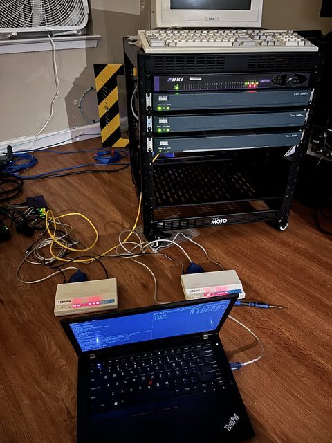The complete setup: rack in the background, ThinkPad laptop on the floor in front, flanked by two Cisco VoIP/POTS adapters