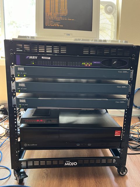 Equipment rack containing the MRV switch, three Cisco 2600 routers, and a SilverStone PC, with a CRT monitor in the background